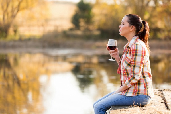 thoughtful young woman with glass of wine on pier in autumn