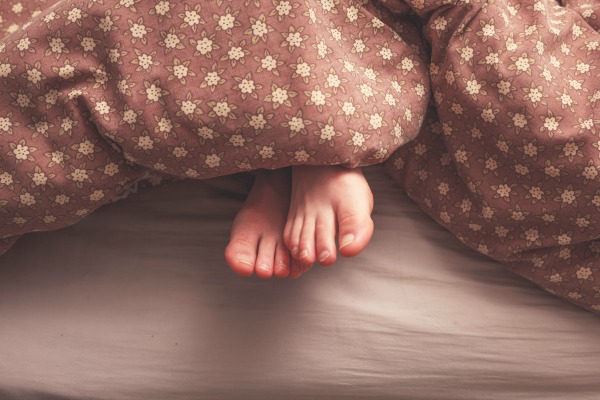 Young woman's feet in bed under the covers